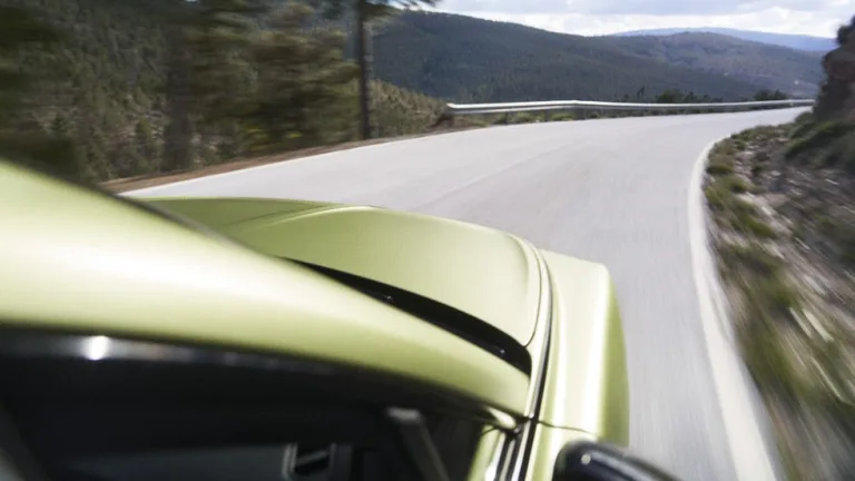 A green car speeding along a winding road through a scenic mountainous landscape. A green car speeding along a winding road through a scenic mountainous landscape.