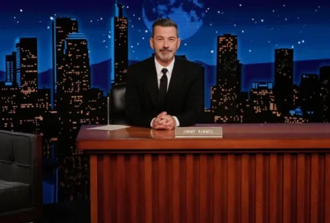 ABC host Jimmy Kimmel sitting at his desk on the set of his show.