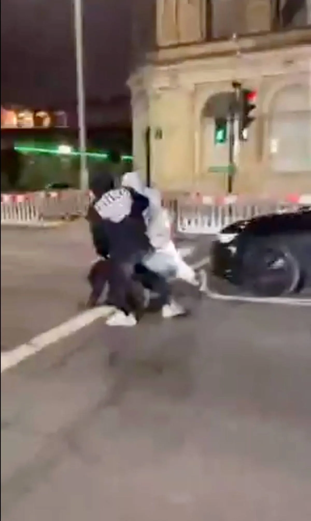 Image 5: An individual is seen attempting to assist another individual in a street setting, with a vehicle and illuminated structures in the background.