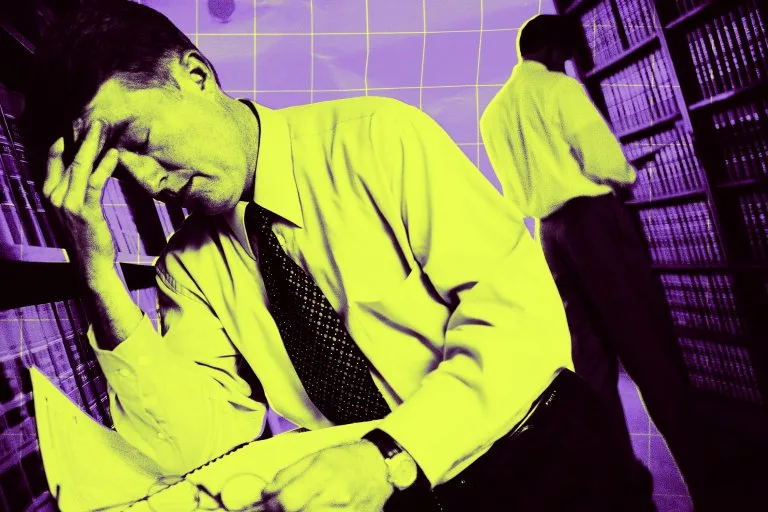 Image 6: A man in a dress shirt and tie is sitting and holding his head in his hand, appearing stressed or deep in thought, while looking at an open binder. Another man in similar